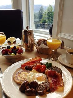 a breakfast plate with eggs, bacon, fruit and toast on the table next to a glass of orange juice