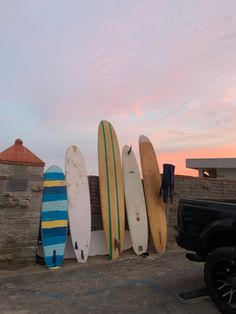 several surfboards are lined up against a stone wall in front of a black truck