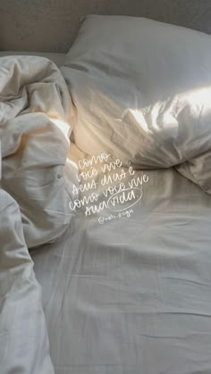 an unmade bed with a white comforter and some words on the pillowcase