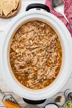 a white crock pot filled with beans and tortilla chips on top of a wooden table