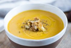 a white bowl filled with yellow soup on top of a wooden table next to a napkin