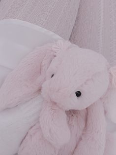 a pink teddy bear sitting on top of a bed next to a white comforter