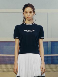 a woman standing in front of a tennis court wearing a black shirt and white skirt