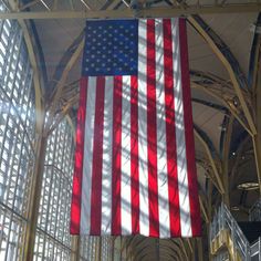 an american flag hanging from the ceiling in a train station with sunlight streaming through it