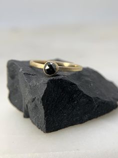 a gold ring with a black diamond on top of a piece of rock in front of a white background