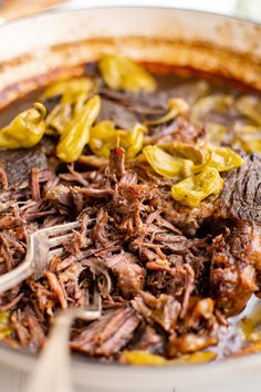 a white bowl filled with meat and vegetables on top of a table next to a fork