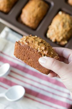 a hand holding a piece of bread in front of muffins