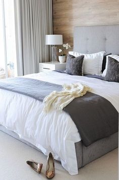 a bed with white and gray sheets, pillows and blankets on top of it next to a window