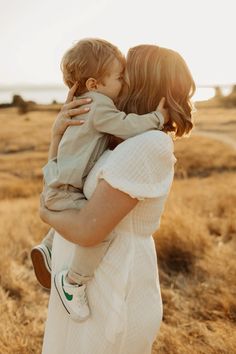 a woman holding a small child in her arms while standing on a dry grass field