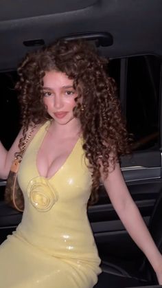 a woman in a yellow dress is sitting in the back of a car and posing