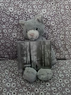 a stuffed animal with a book on it's lap sitting in front of a floral wallpaper