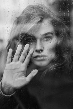 a woman holding her hand up to her face in front of a rain soaked window