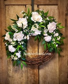 a wreath with white flowers and greenery hangs on a wooden door, ready to be hung