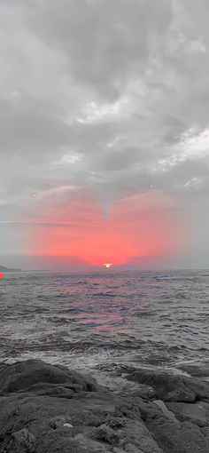 the sun is setting over the ocean with rocks