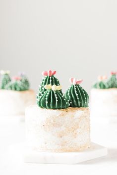 three small cactus shaped cakes sitting on top of a white cake plate with pink bows