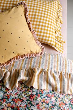 a bed topped with lots of pillows next to a wall covered in yellow and white checkered sheets