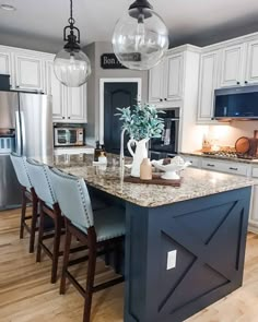 a kitchen with white cabinets and marble counter tops, an island in the middle is surrounded by blue bar stools