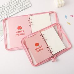 two pink notebooks sitting on top of a desk next to a keyboard and mouse