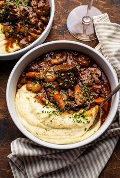 two bowls filled with mashed potatoes and beef stew next to a glass of wine