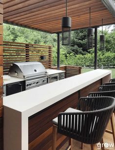 an outdoor kitchen with grill and bar stools under a pergolated roof area