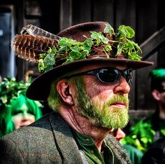 a man with green hair wearing a brown hat and sunglasses, standing in front of other people