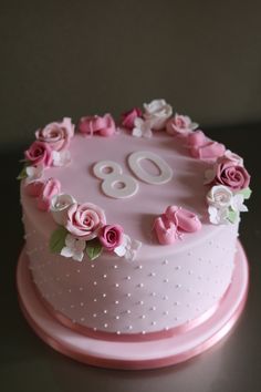 a pink birthday cake with white and pink flowers on the top is decorated with an 80