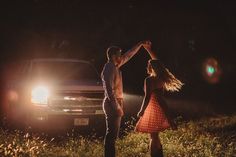 a man and woman dancing in front of a truck at night with their arms around each other