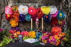 a table topped with lots of colorful flowers next to a wall covered in paper flowers