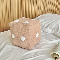 a large pink dice sitting on top of a bed next to a rolled up newspaper