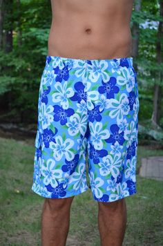 a man standing in the grass wearing blue and green floral swim trunks with no shirt on