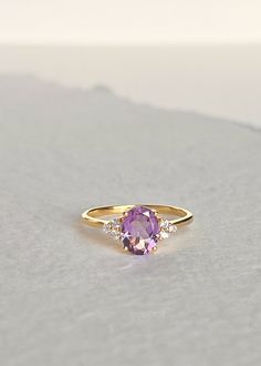 Our Fleur Amethyst ring features a single soft purple faceted Amethyst stone set in a sturdy four-prong setting surrounded with three white topaz on each side. It can be worn as an engagement ring and a statement ring stacked with our Colline and Hana ring for a unique look. Always handmade with genuine and natural stones on solid sterling silver and thick gold vermeil that will stand the test of time. D E T A I L S * Materials - 18k gold vermeil on solid 925 sterling silver, genuine faceted Ame Modern Amethyst Ring As Gift, Timeless Purple Rings As Gifts, Timeless Purple Rings Perfect For Gifts, Timeless Purple Rings For Gifts, Timeless Amethyst Ring As A Gift, Timeless Oval Amethyst Ring As Gift, Timeless Oval Amethyst Ring For Gift, Minimalist Jewelry With Center Stone, Modern Yellow Gold Amethyst Ring With Accent Stones