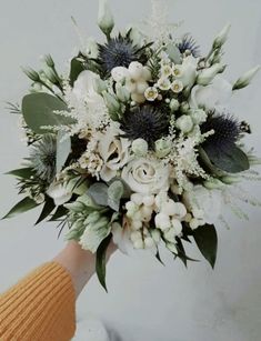 a bridal bouquet with white flowers and greenery is held by someone's hand