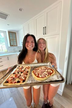 two young women holding trays of pizza in the kitchen