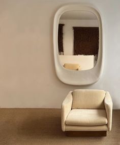 a white chair sitting in front of a mirror on the wall next to a couch