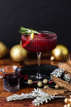 a red drink in a glass on top of a wooden table next to christmas decorations