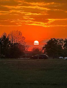 the sun is setting over a field with cars