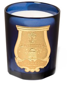 a blue and black glass candle with a gold emblem on the top, in front of a white background