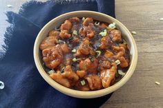 a bowl filled with meat and vegetables on top of a wooden table next to a blue napkin