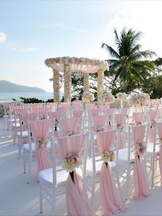 rows of white folding chairs with pink sashes and flowers on them at an outdoor wedding ceremony