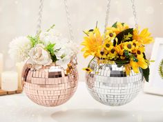 two disco ball vases with sunflowers and daisies in them hanging from chains