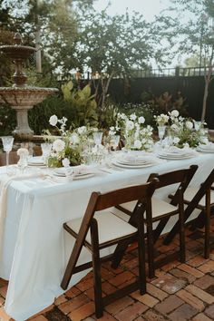 a long table with white flowers and plates on it is set for an outdoor dinner