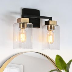 two lights are attached to the wall in front of a mirror and potted plant