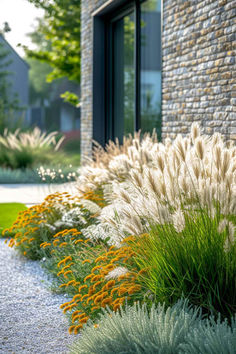 some very pretty plants by the side of a brick building with large windows and grass