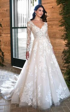 a woman standing in front of a wooden wall wearing a wedding dress with long sleeves