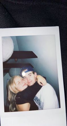 a man and woman hugging each other in front of a black background with a polaroid frame