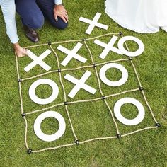 a man and woman sitting on the grass next to an outdoor tic - tac - toe game