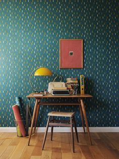 a desk with a chair and lamp in front of a wallpapered wall that has an old typewriter on it