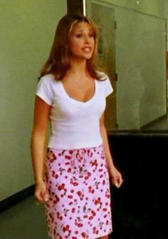 a woman standing in front of a mirror wearing a white shirt and pink floral skirt