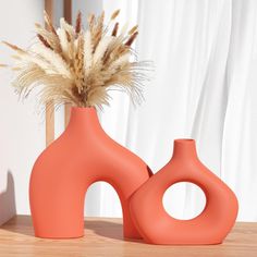 two orange vases sitting on top of a wooden table next to a mirror with dried grass in it