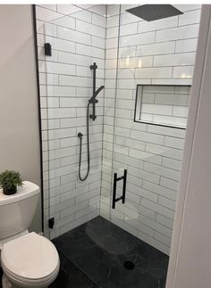 a white toilet sitting next to a walk in shower with black tile on the floor